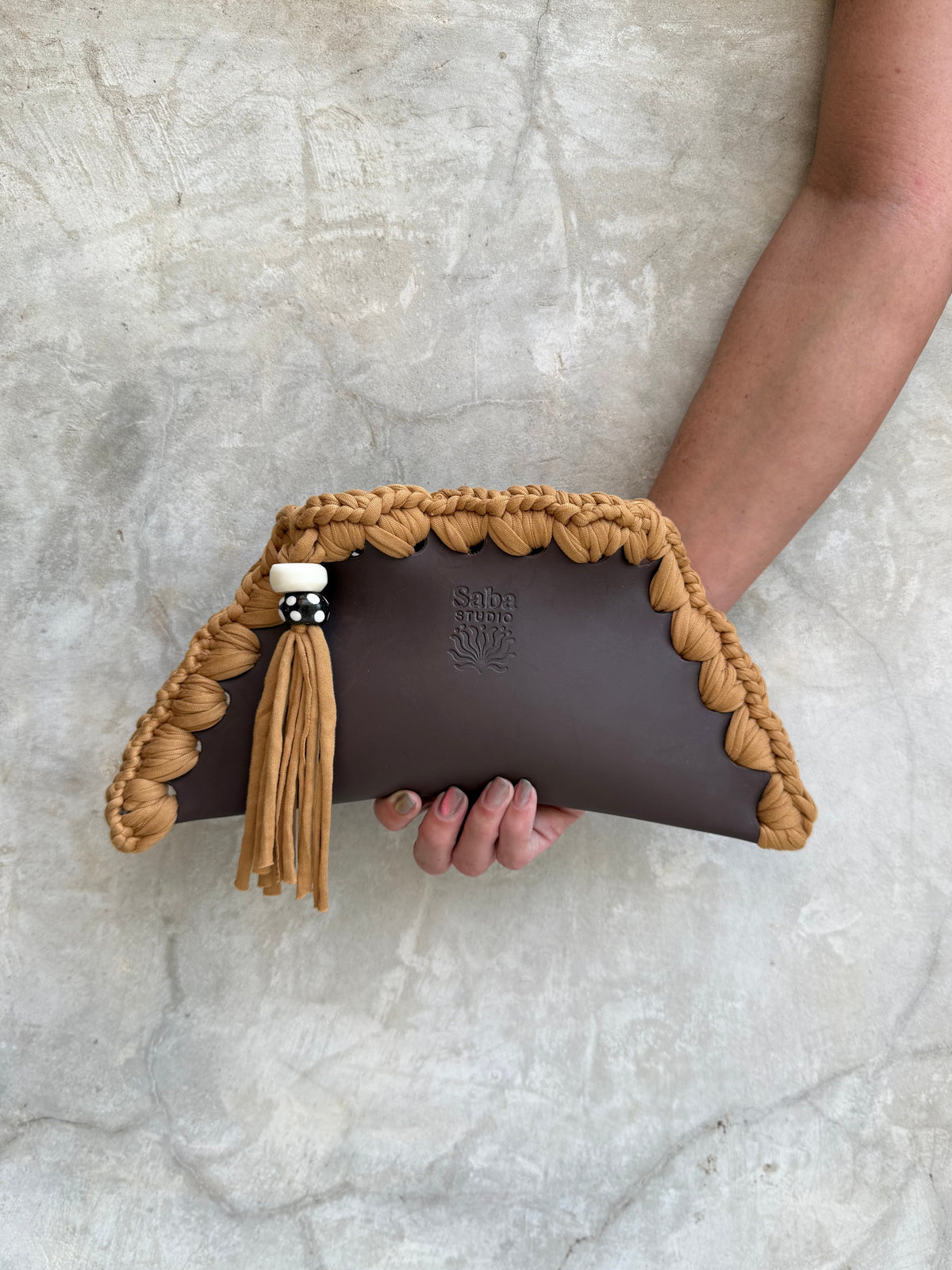 Kora clutch photographed against a natural grey wall, full view