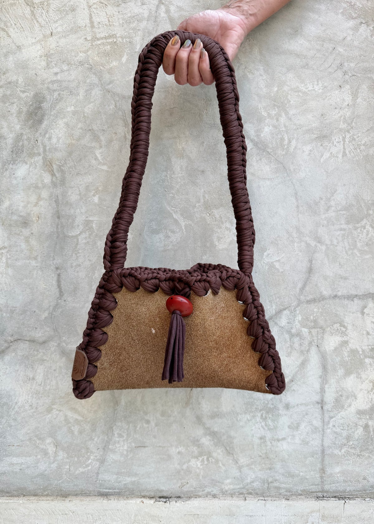 Solara shoulder bag with purple trim and red bead, full view against a natural grey wall
